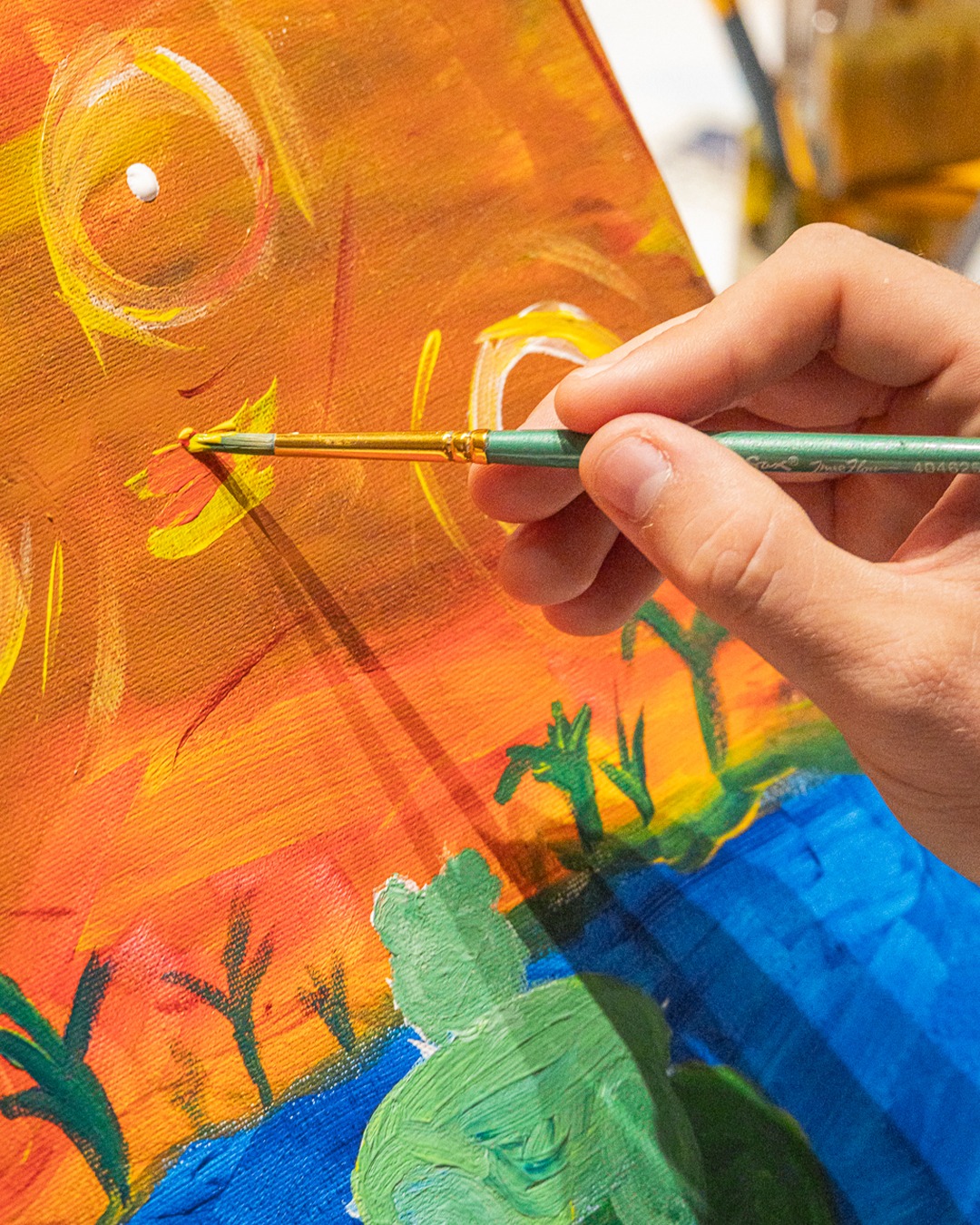 Close-up of a paintbrush adding detail to a frog canvas at the Puff N Paint class