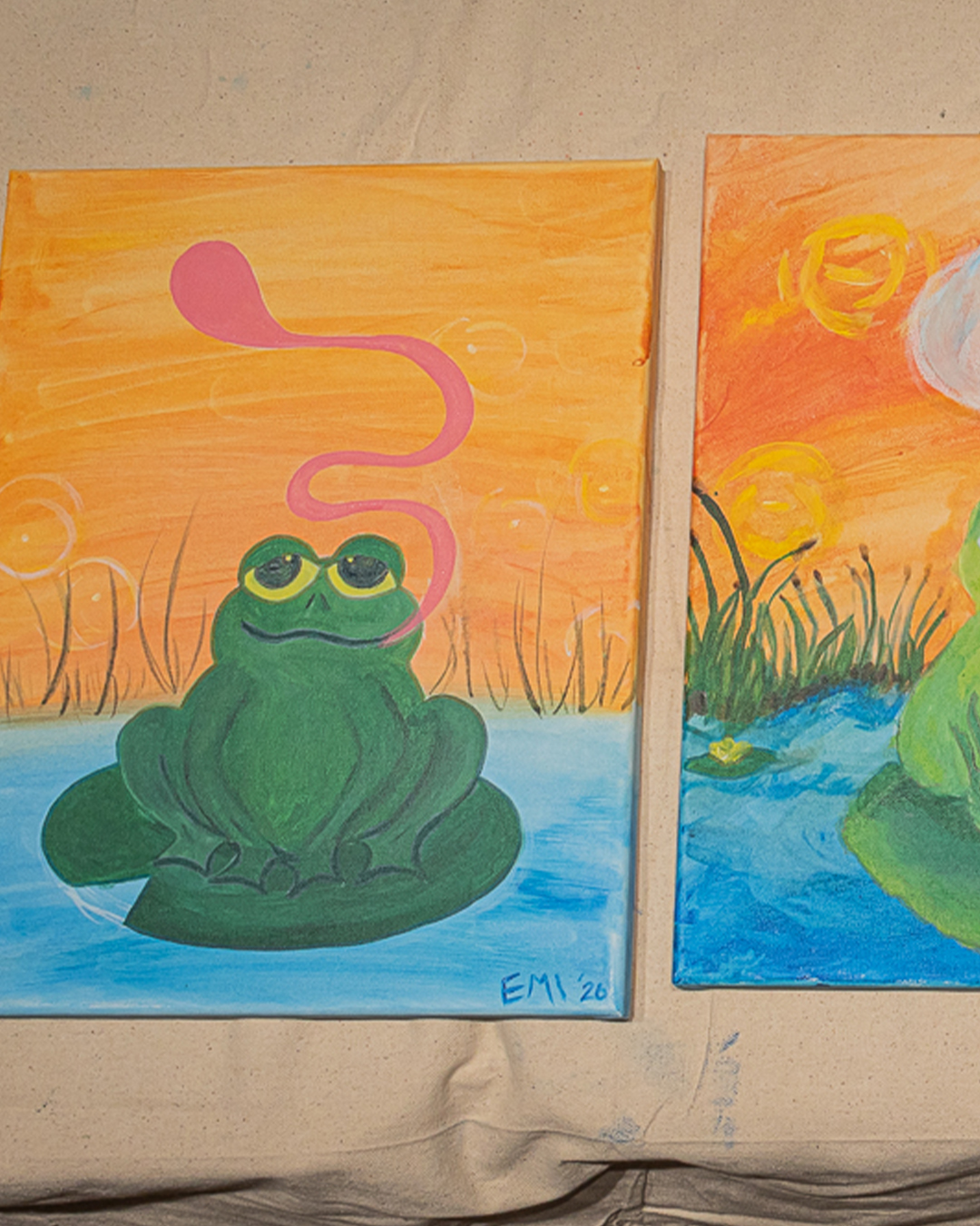 Finished frog paintings lined up on the wall after the Puff N Paint class
