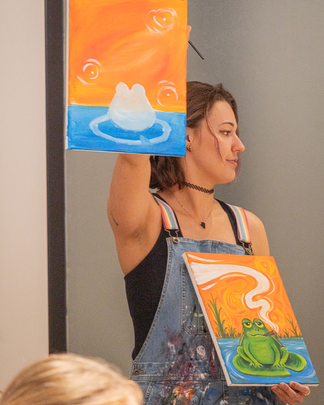 Guest holding up her finished frog painting at the Puff N Paint class at 6 Point Flower Shop